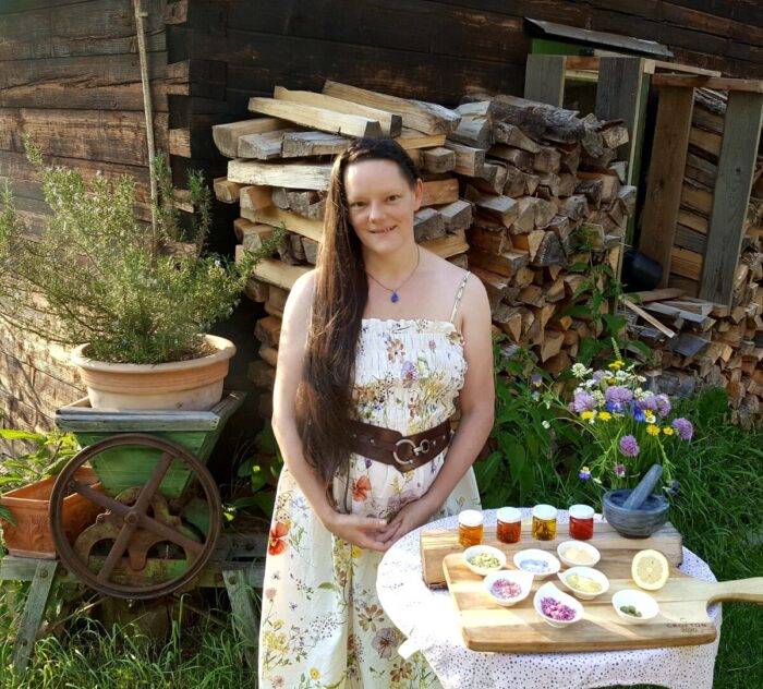 Sylvana Kuhl mit Kräutermaterial, Gläsern und Schälchen am Tisch